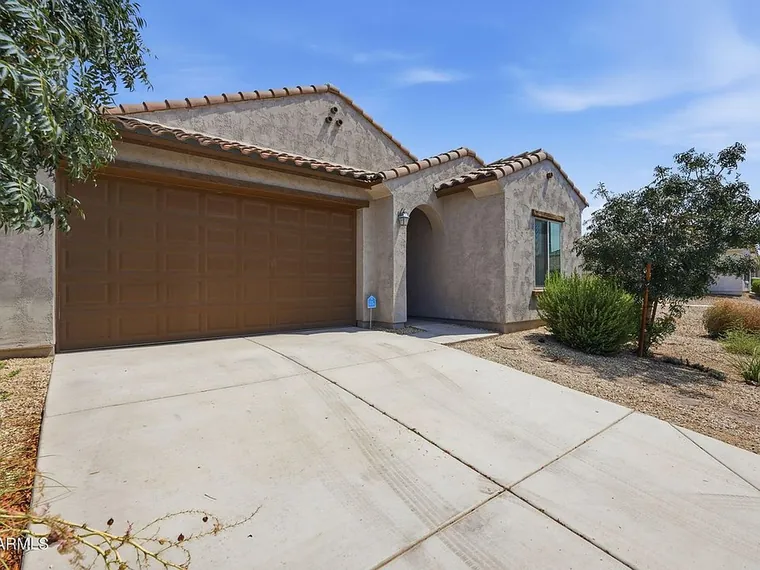 Single story tan stucco home with a tile roof, an arched entry and a brown two-car garage door at 11204 W Mobile Ln, Tolleson, Arizona