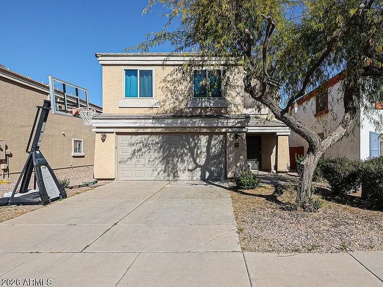 Two story tan stucco home with a two-car garage and a mature desert tree in front at 36536 W Santa Maria St, Maricopa, Arizona