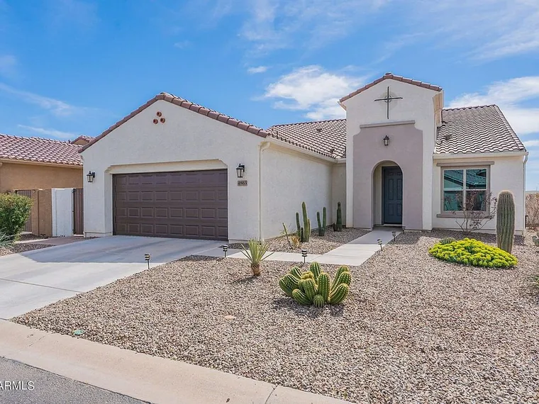 Single story white stucco home with a tile roof, a dark two-car garage door and cactus landscaping at 4863 W Picacho Dr, Eloy, Arizona